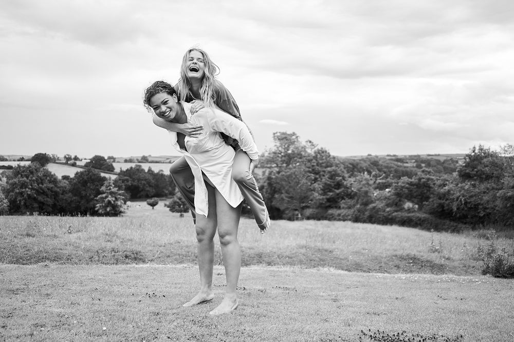 A model giving another model a piggyback in a field wearing pyjamas